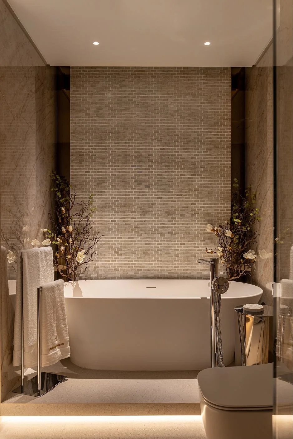 Freestanding bathtub against a pearl-effect mosaic wall in the master bathroom